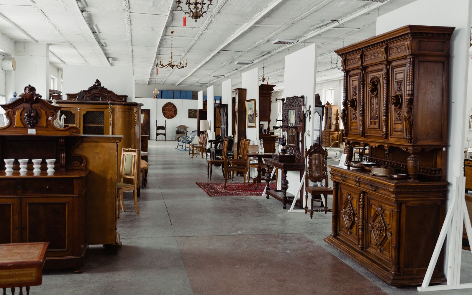 A sunlit aisle of the shop lined with carved-wood cabinets, chairs, and antique furniture